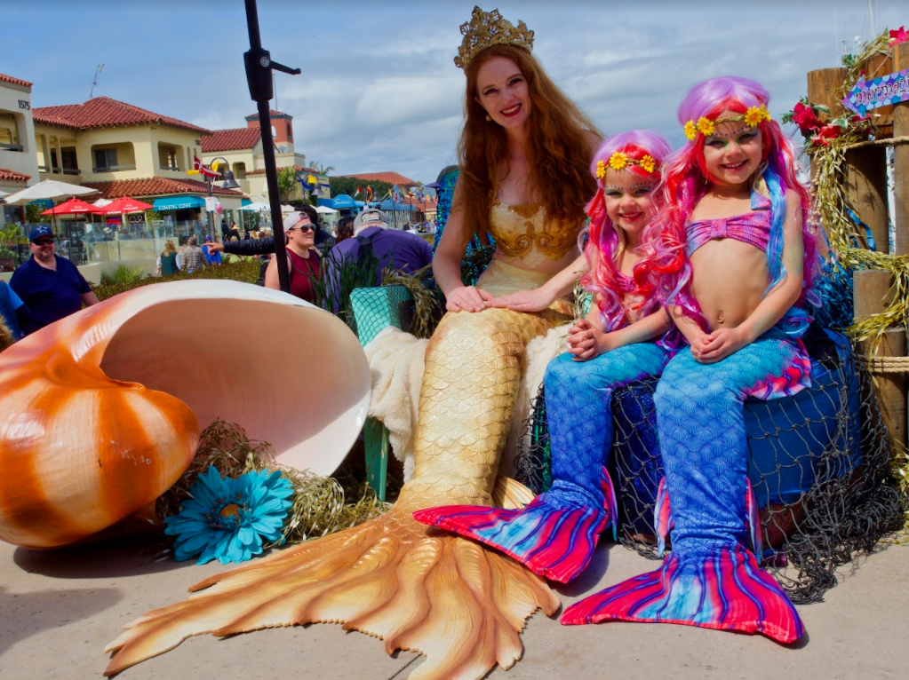 An adult mermaid sitting with two little merfolk for a photo op