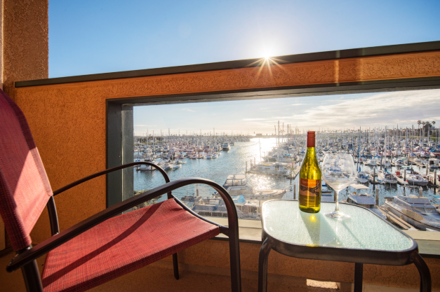 Photo of a table and chair, with wine bottle and empty wine glass on a hotel balcony overlooking the Ventura Harbor