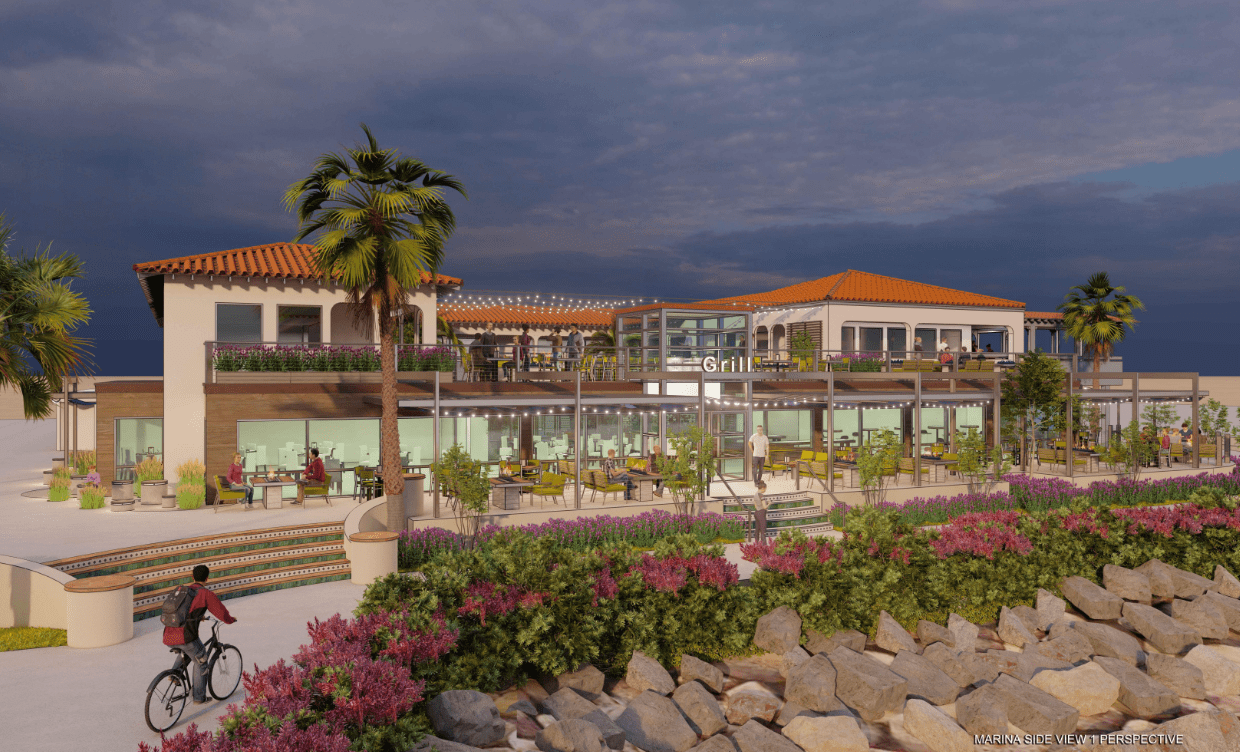 A two-story waterfront restaurant with outdoor seating, palm trees, and a cyclist on a pathway in the foreground under a cloudy sky.